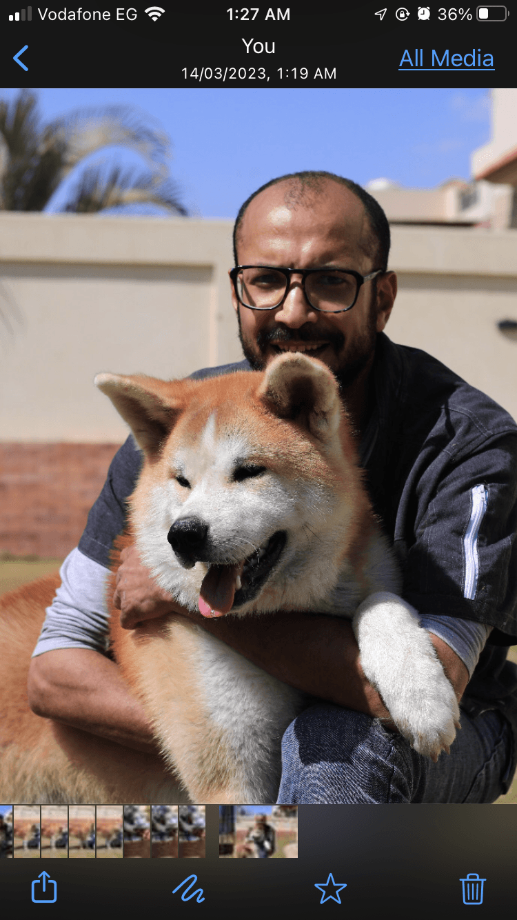 Smiling man with glasses hugging a large, fluffy orange and white Akita dog outdoors.